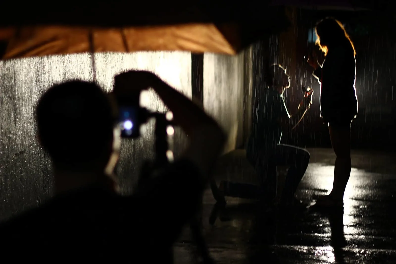 Ein Mann macht ein Foto von einem Paar, das während eines Vorschlags unter Regenschirm auf dem Regen steht