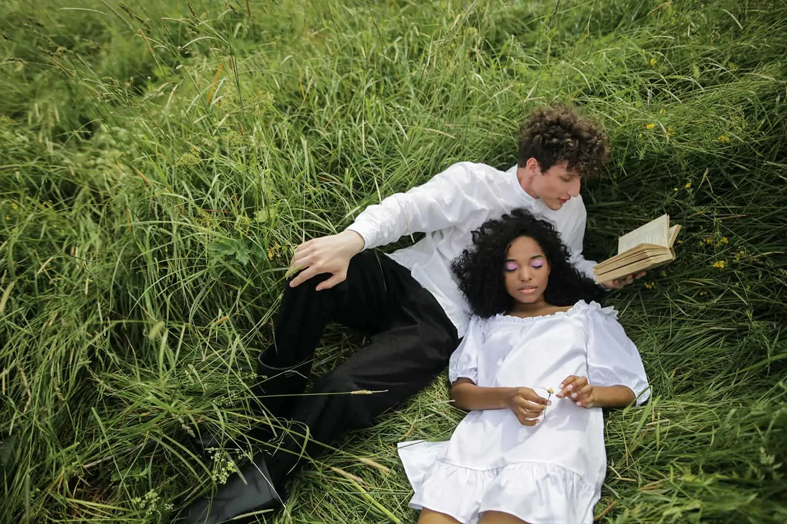 Ein Mann liest einer Frau ein Liebesgedicht vor, während er zusammen in einem grünen Gras liegt