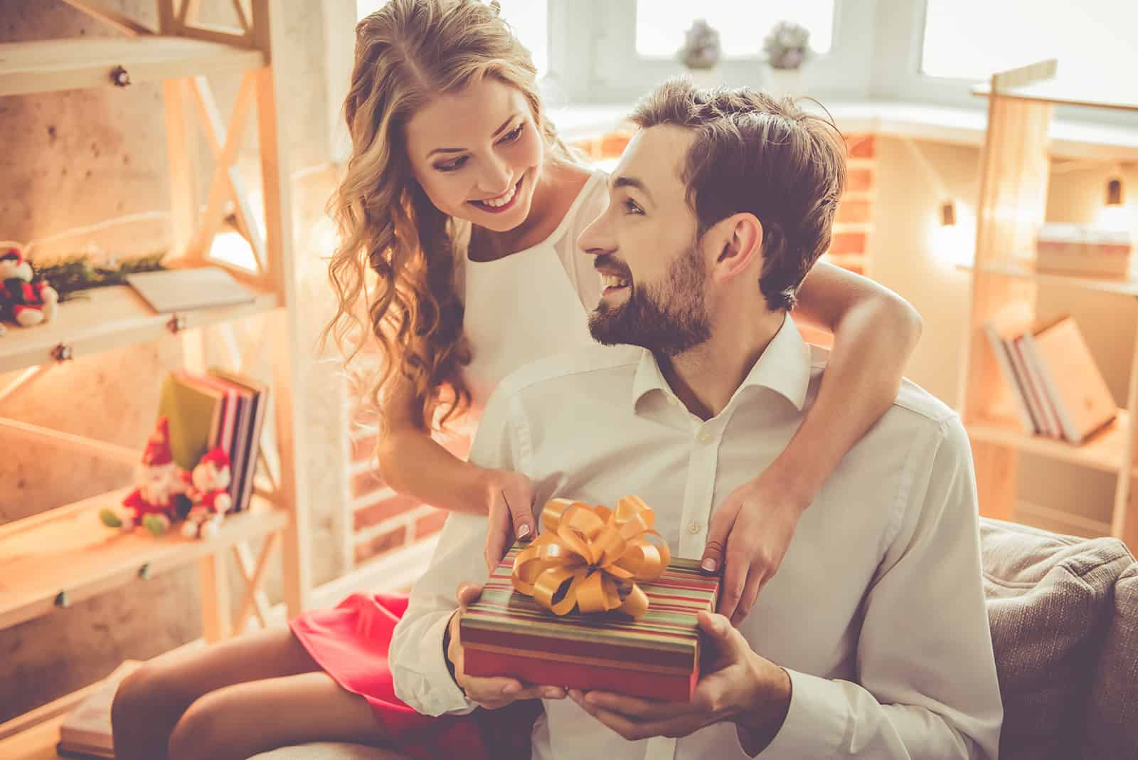 Ein lächelnder Mann erhält ein Geschenk von seiner Freundin zu Hause