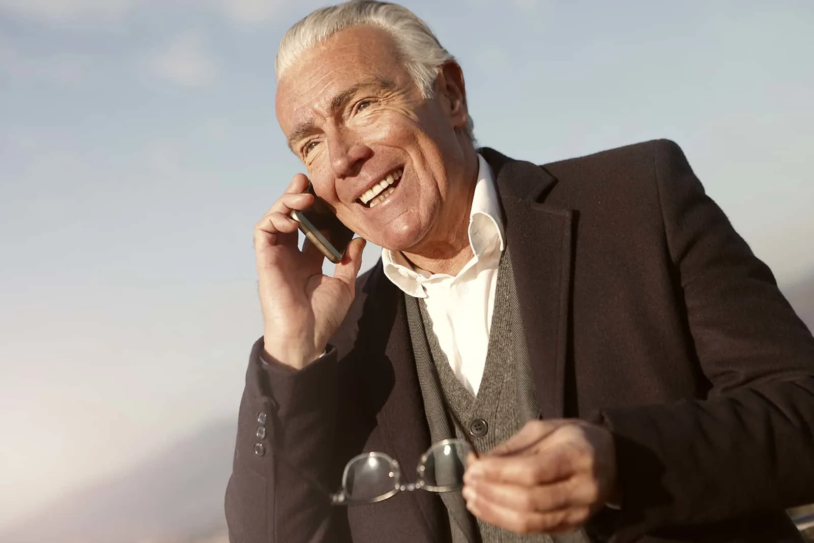 ein lächelnder älterer Mann, der einen Anruf hat, während er Brillen in der Hand hält