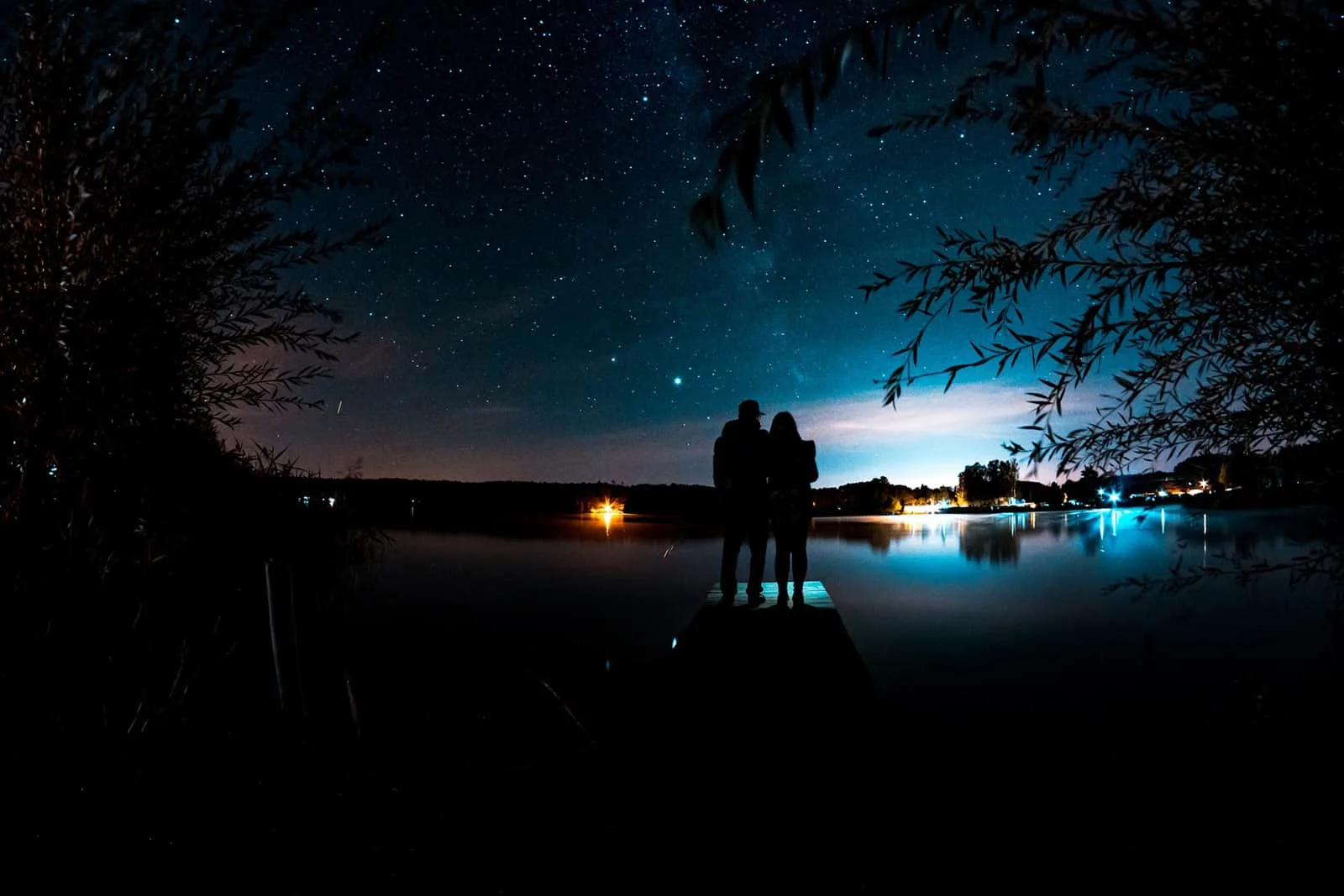 Ein liebevolles Paar beobachtet Sterne, die auf einem Dock in der Nähe des Gewässers stehen