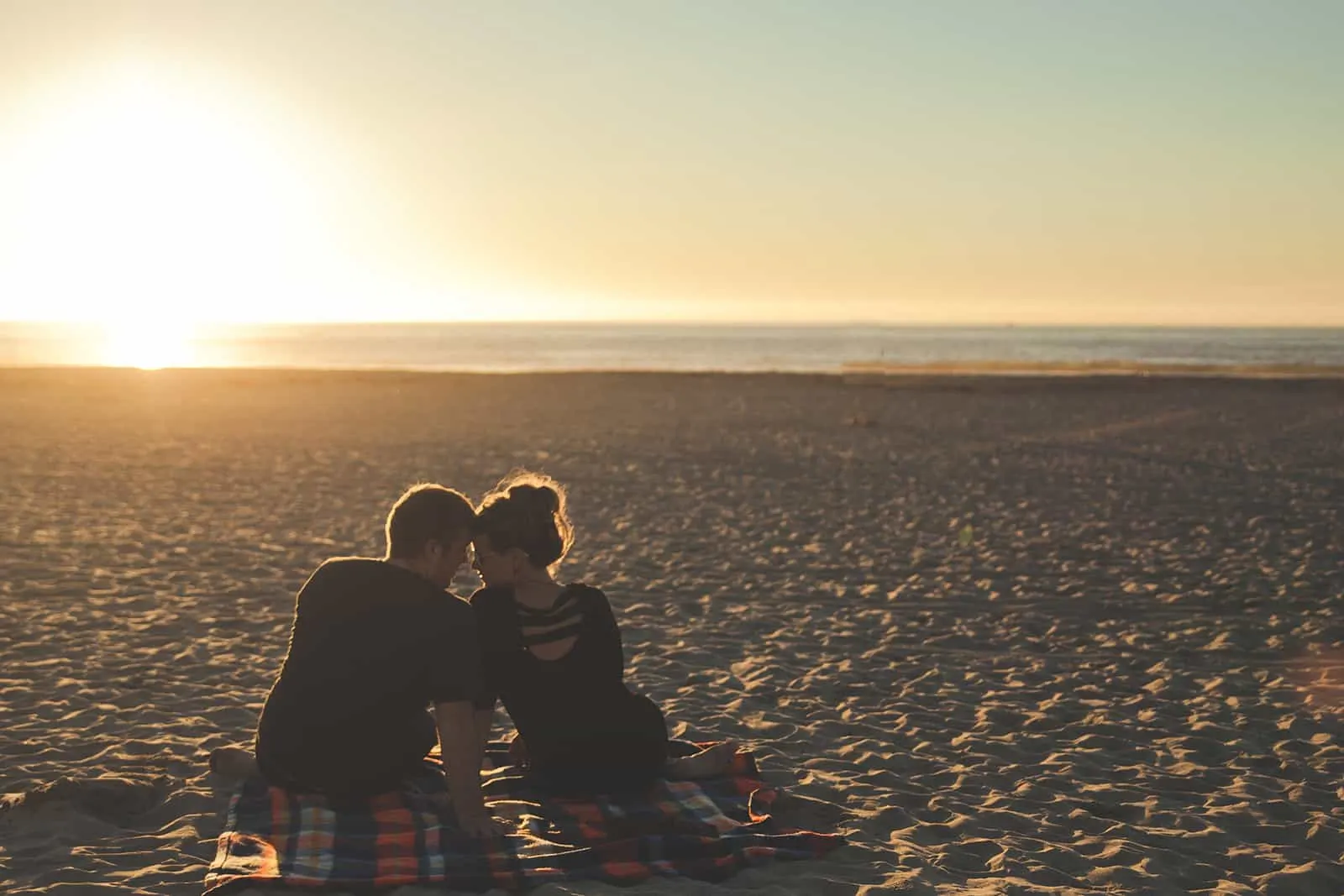 ein liebendes Paar, das während des Sonnenuntergangs am Strand sitzt