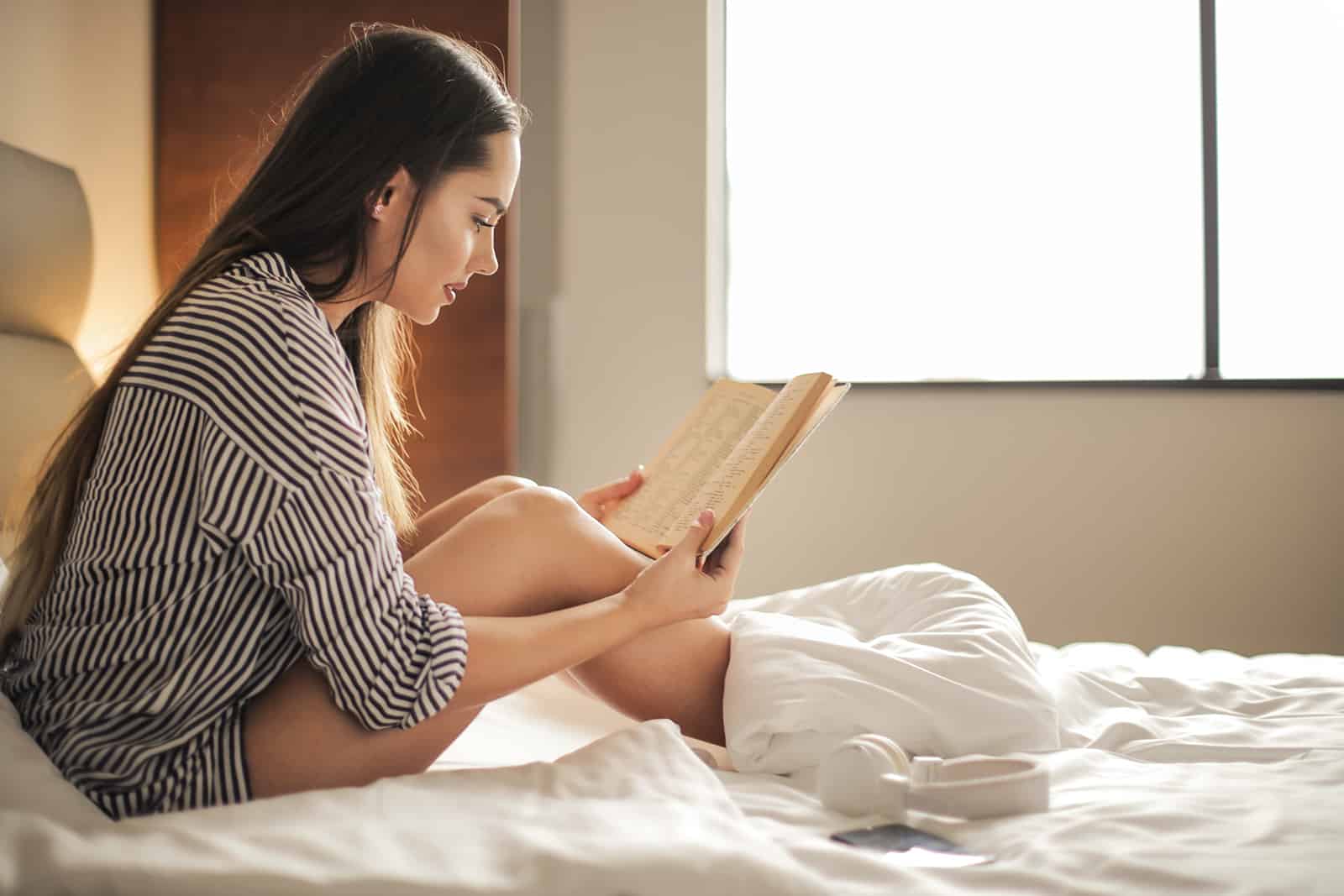 eine Frau, die ein Buch liest, das auf dem Bett sitzt