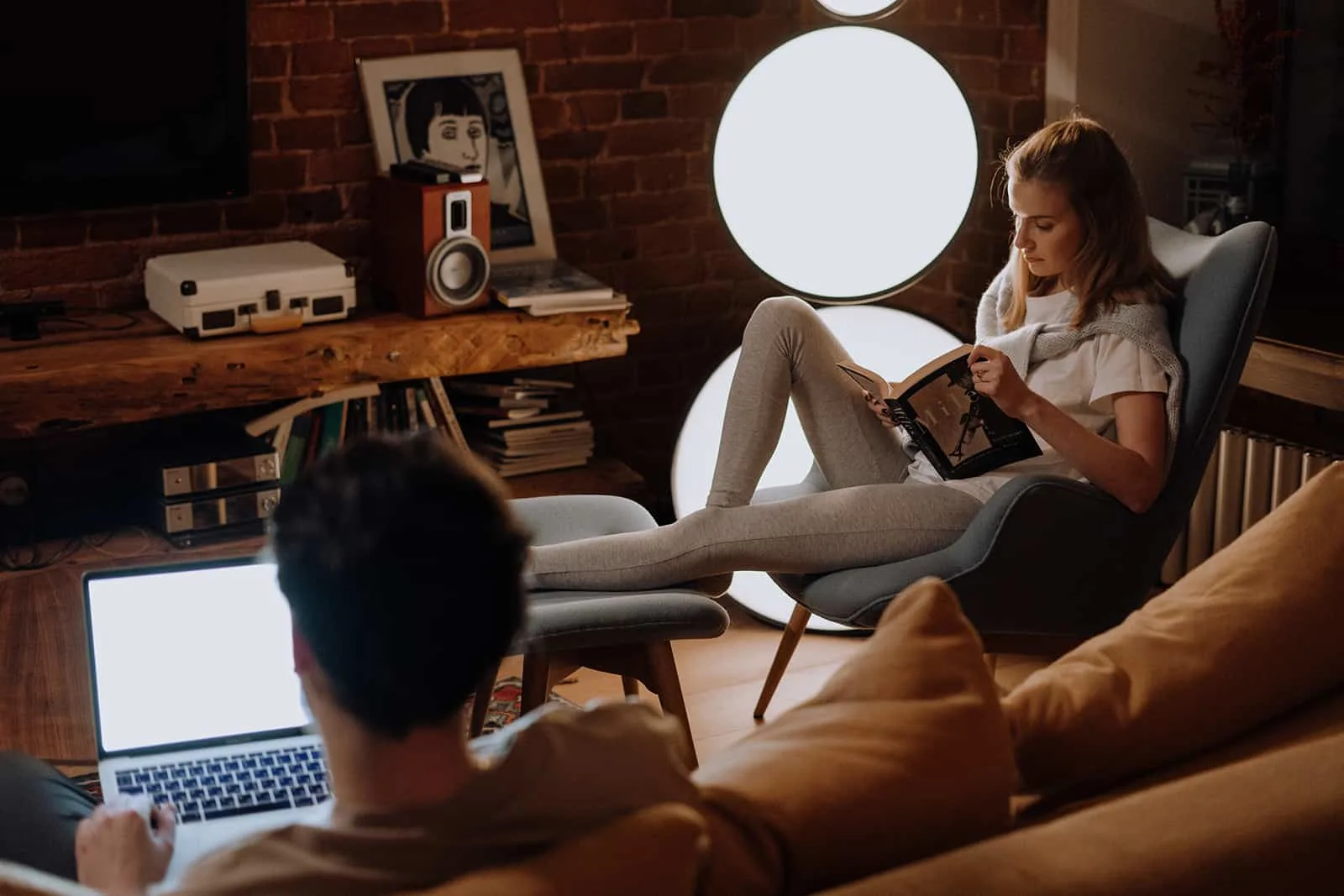 eine Frau, die ein Buch liest, während ein Mann einen Laptop im Wohnzimmer benutzt