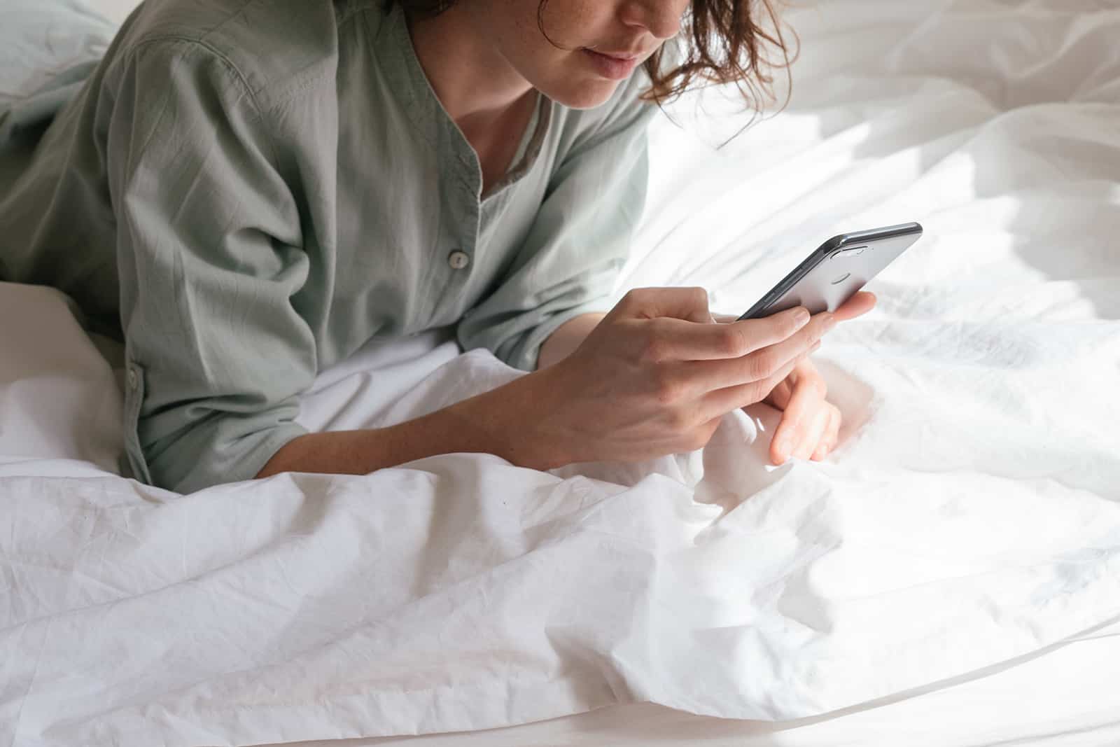 eine Frau, die eine Nachricht auf dem Smartphone tippt, das auf dem Bett liegt