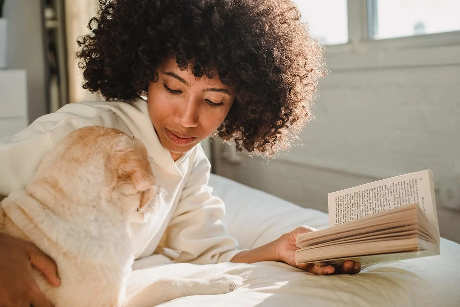 Eine Frau, die einen Hund streichelt, während sie ein Buch liest und auf einem Bett liegt