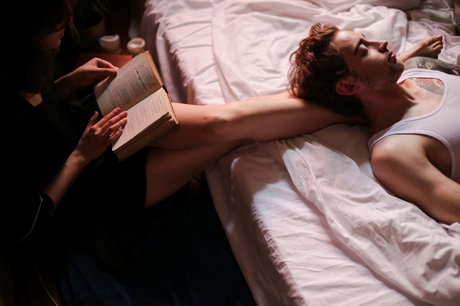 eine Frau, die ihrem Freund, der auf dem Bett liegt, ein Buch vorliest