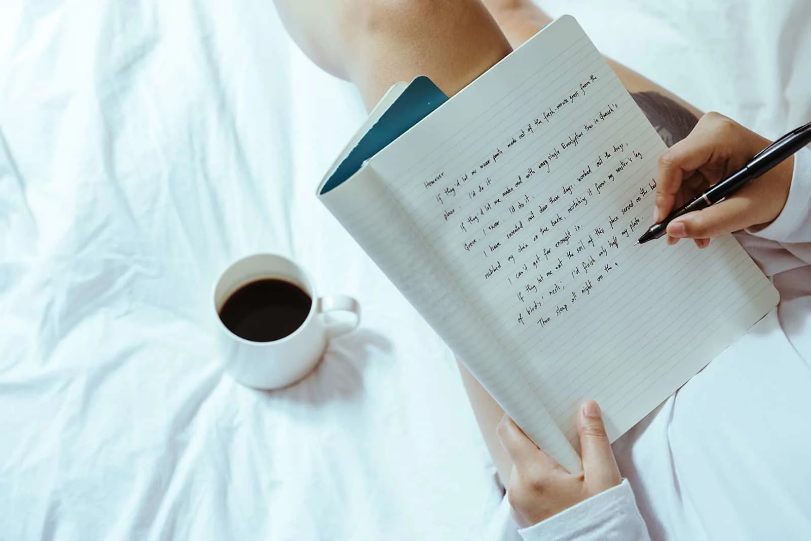 eine Frau, die in ein Notizbuch schreibt, das auf dem Bett sitzt