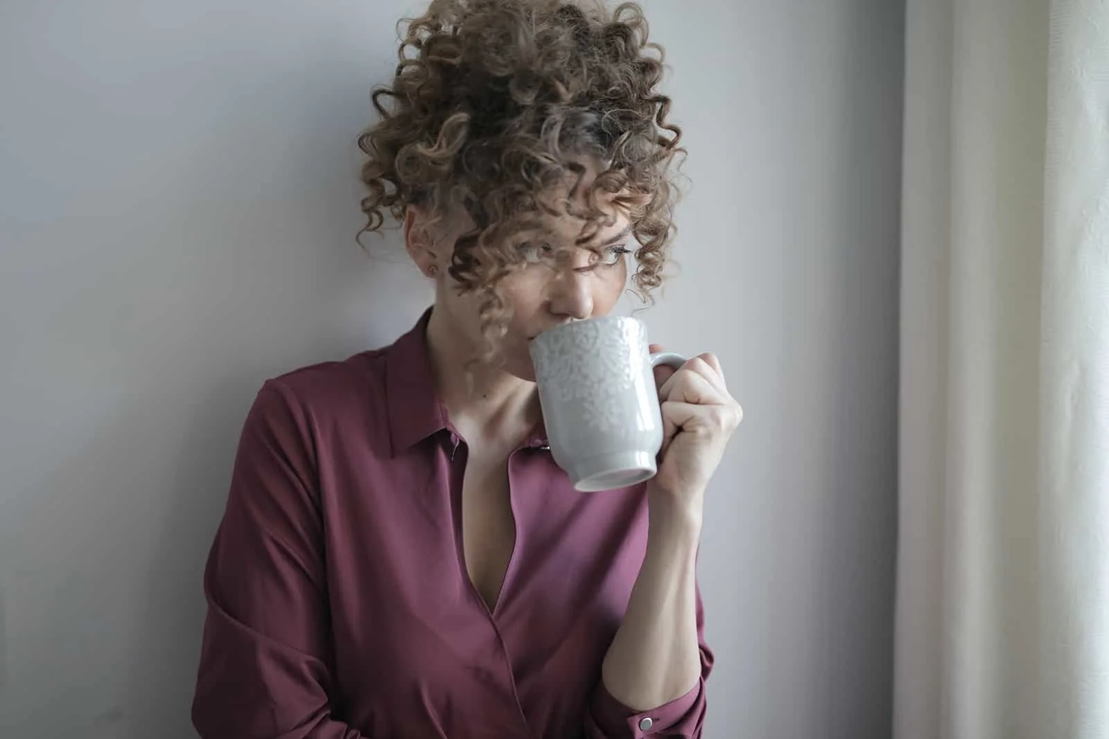 eine Frau, die sich an die Wand lehnt, während sie Kaffee trinkt und nachdenkt