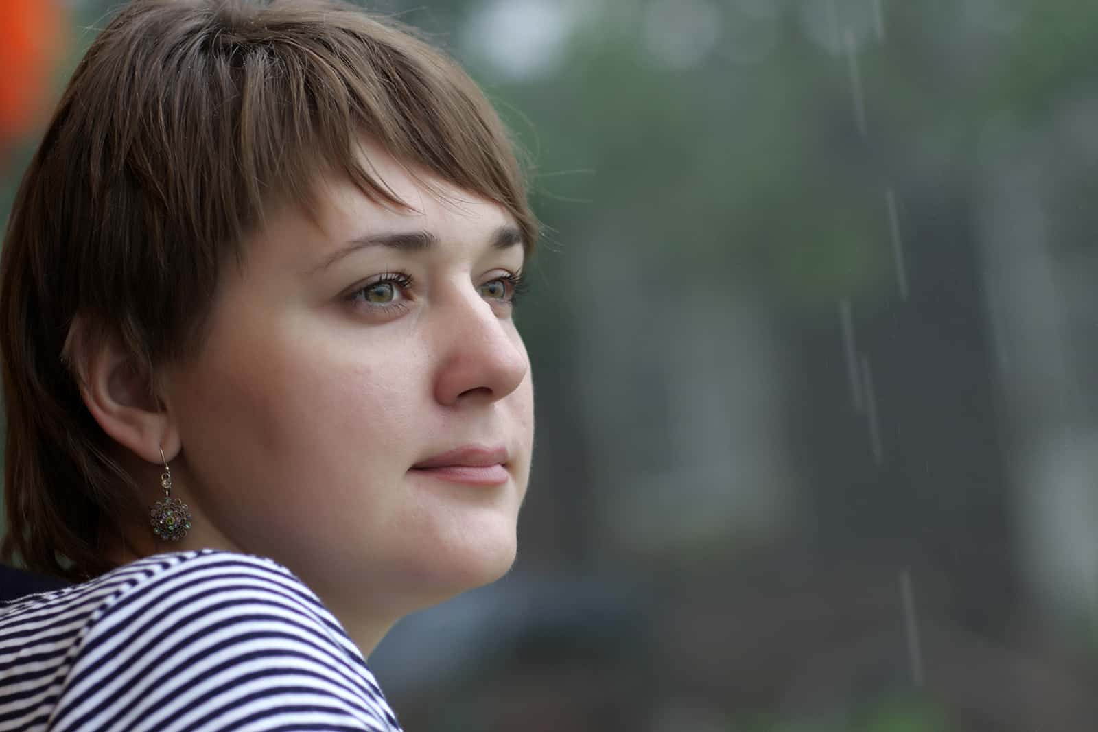 eine Frau mit kurzen Haaren denkt nach, während sie den Regen beobachtet