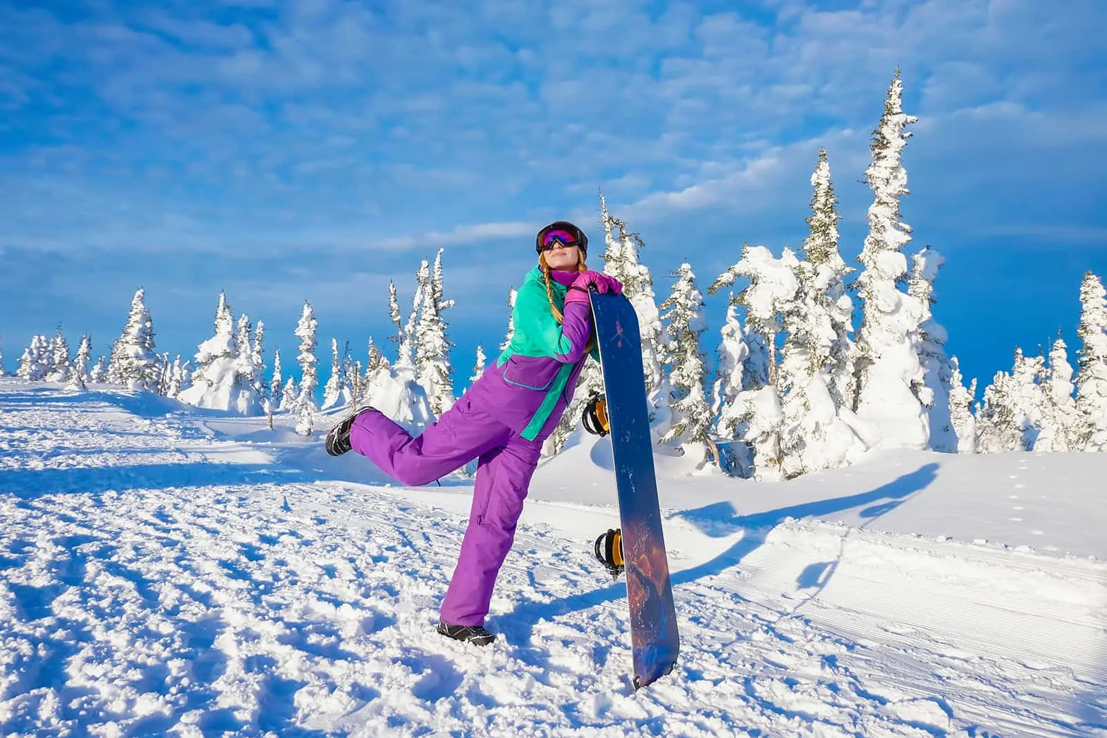 eine Frau, die mit einem Skateboard für Fotografie posiert, während sie auf dem Schnee steht