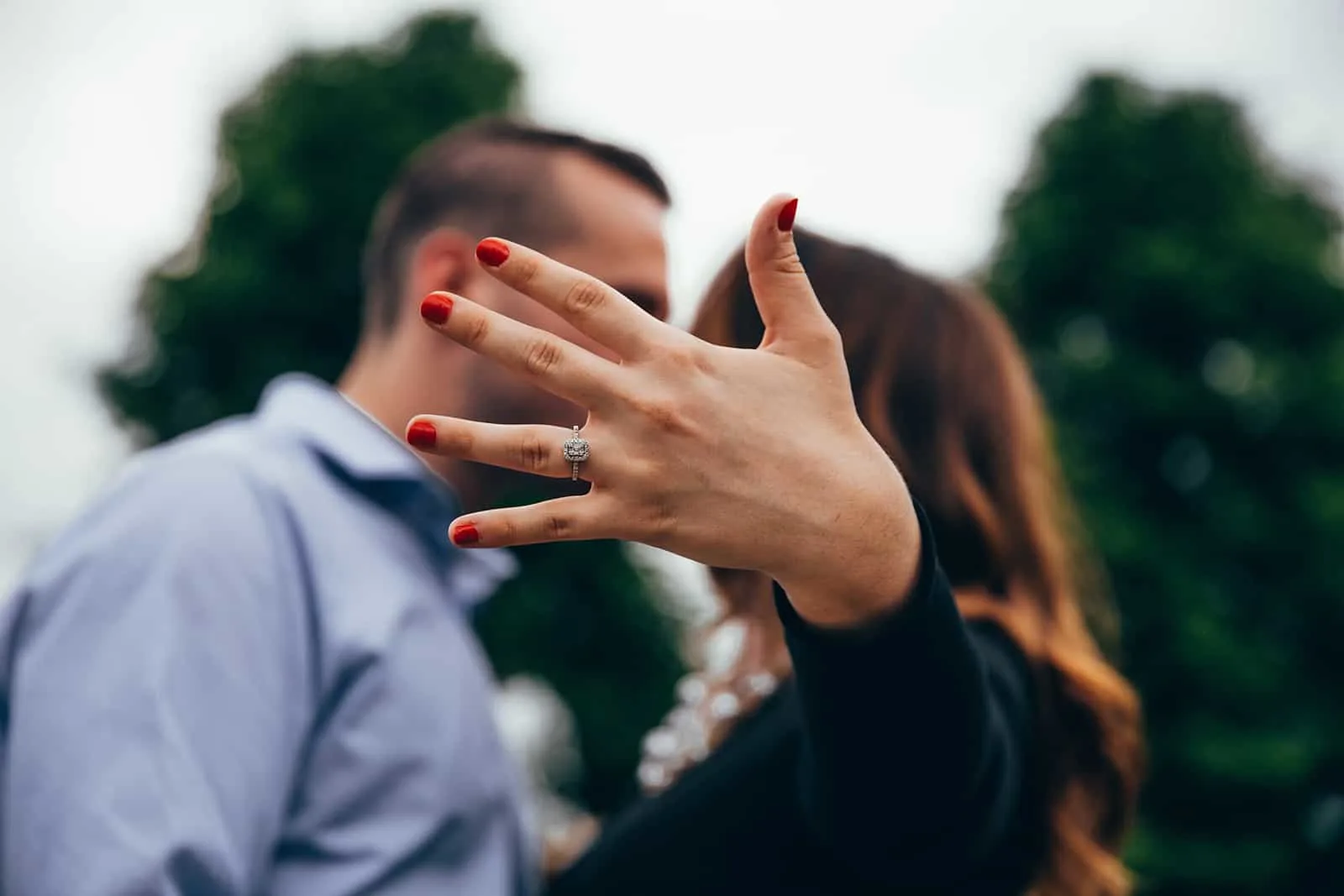 Eine Frau zeigt ihren Ring an einer Hand, während sie sich mit einem Mann küsst