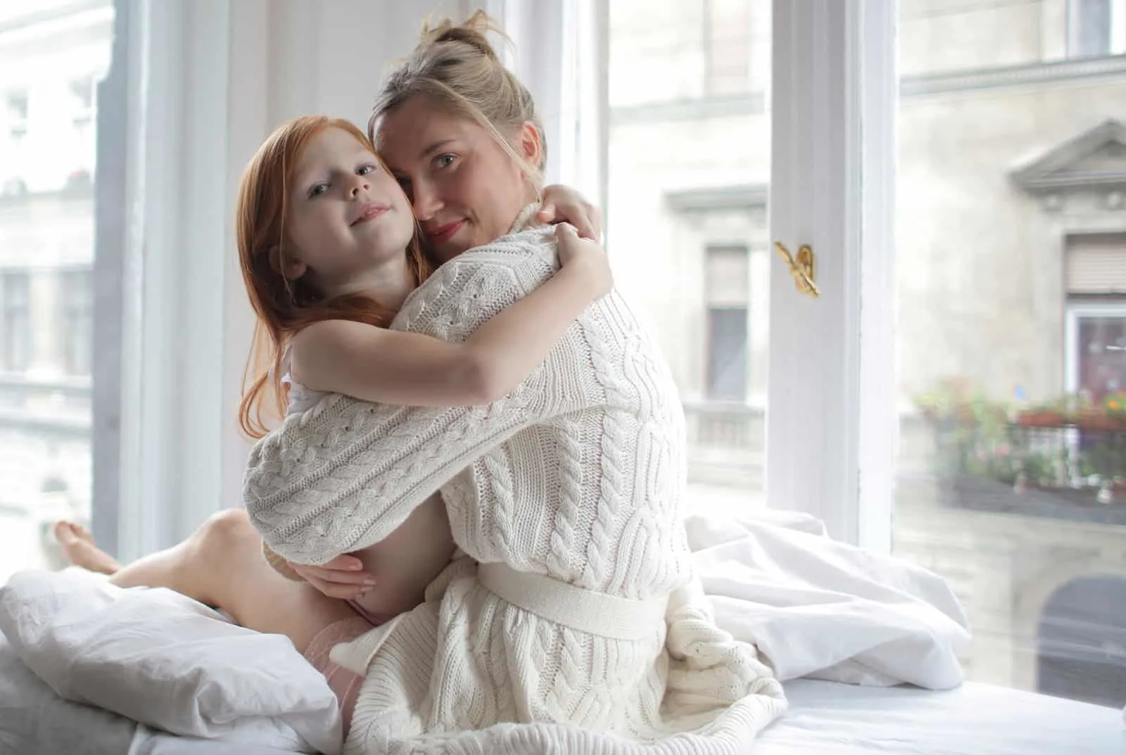 Eine Mutter umarmt ihre kleine Tochter, die auf dem Bett sitzt