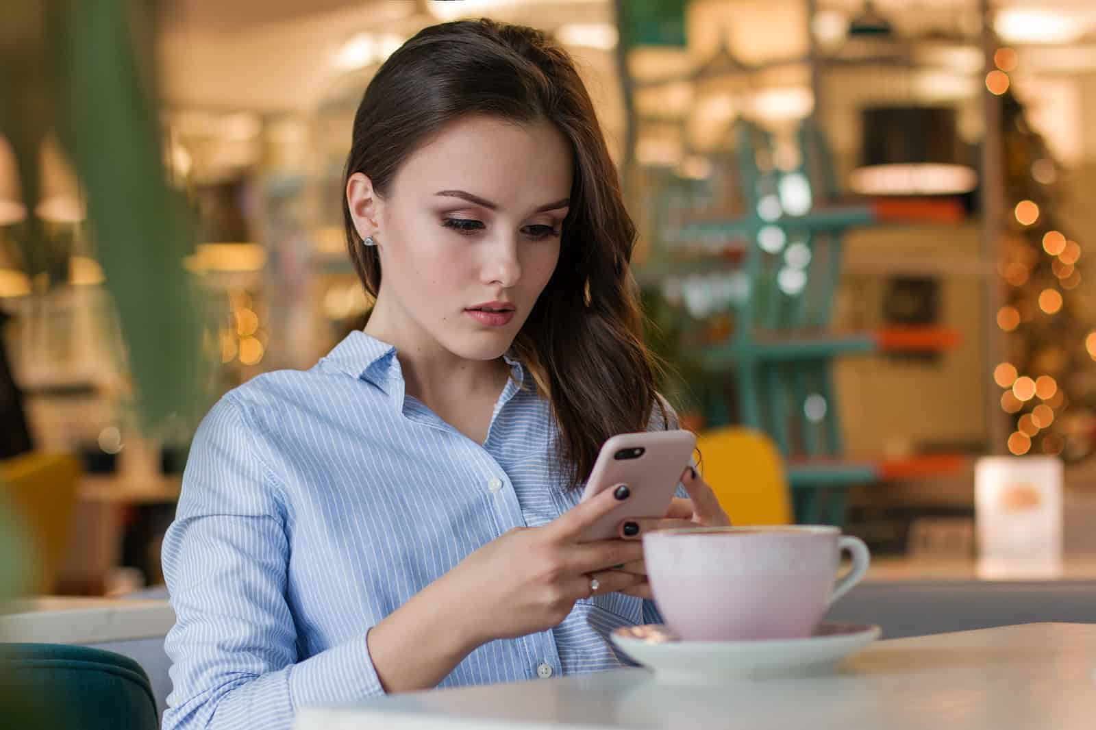 eine besorgte Frau, die auf dem Smartphone tippt, das im Café sitzt