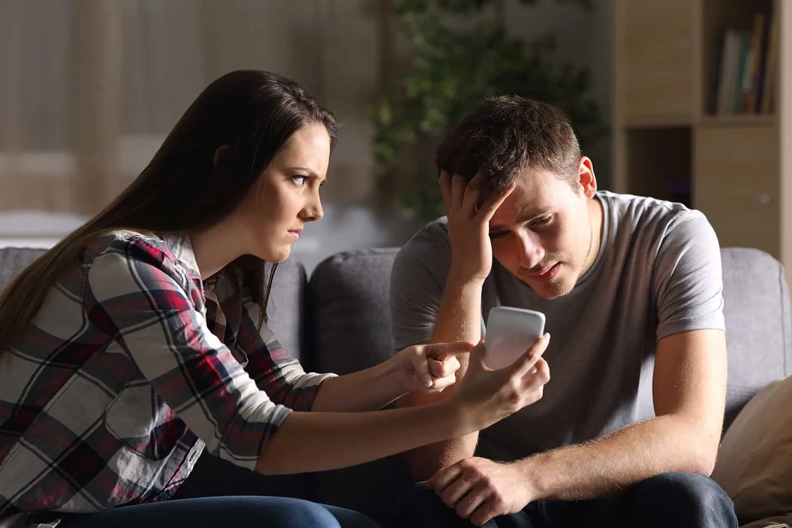 Eine eifersüchtige Frau zeigt ihrem verzweifelten Freund ein Smartphone und bittet um eine Erklärung