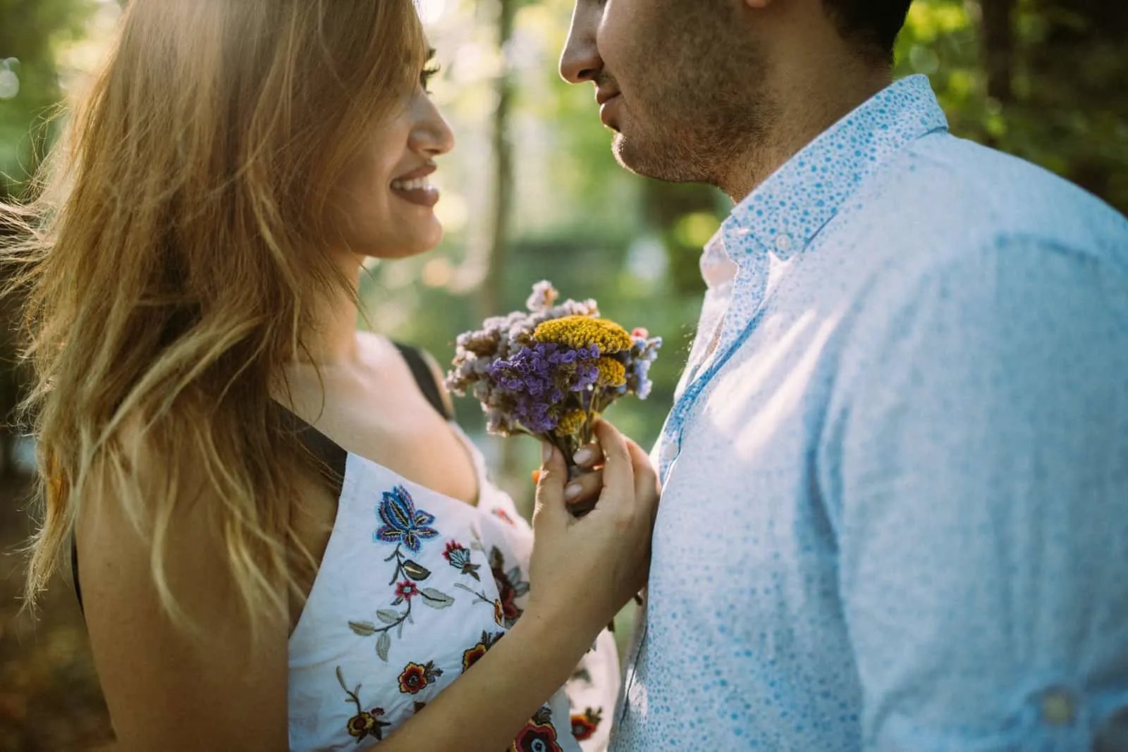 eine lächelnde Frau, die einen Blumenstrauß vor einem Mann hält, der nahe bei ihr steht