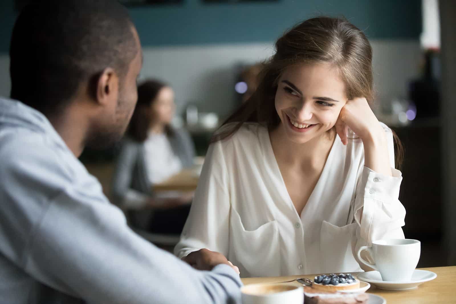 eine lächelnde Frau, die mit einem Mann im Café sitzt und ihm in die Augen schaut