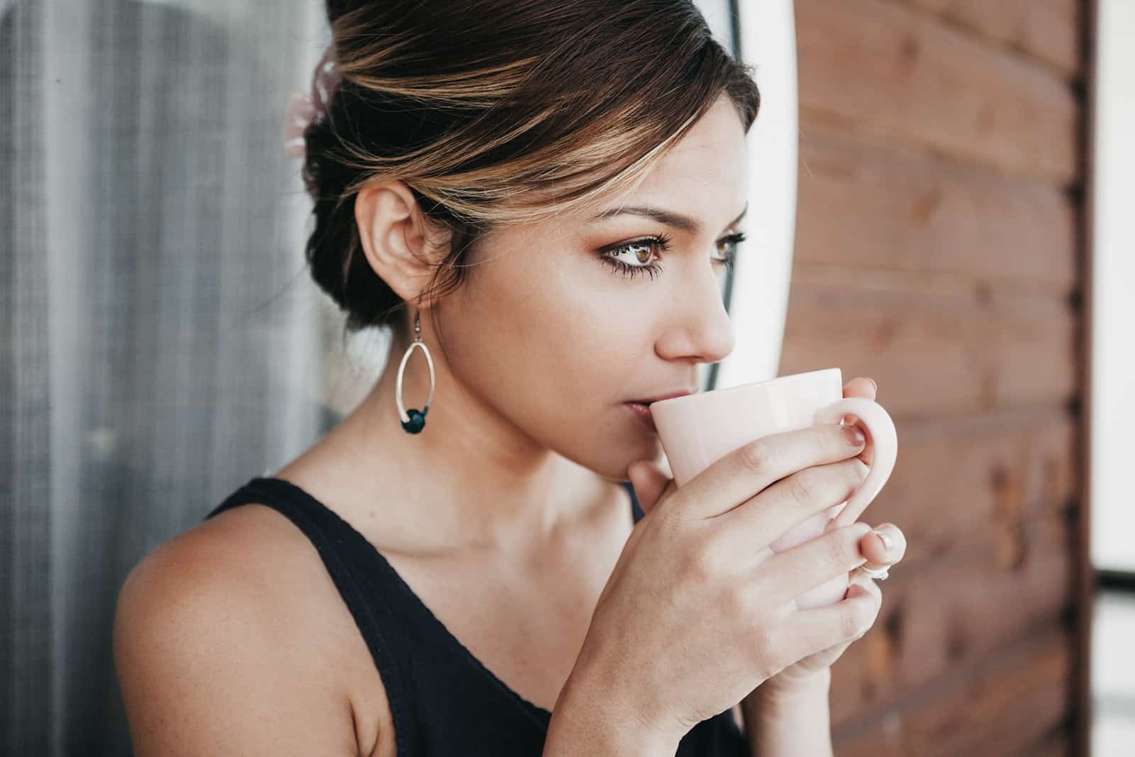 eine nachdenkliche Frau, die auf dem Balkon Kaffee trinkt