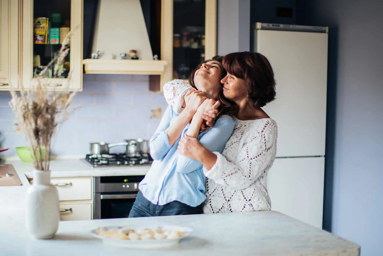 Eine reife Mutter umarmt ihre Tochter und steht in der Küche