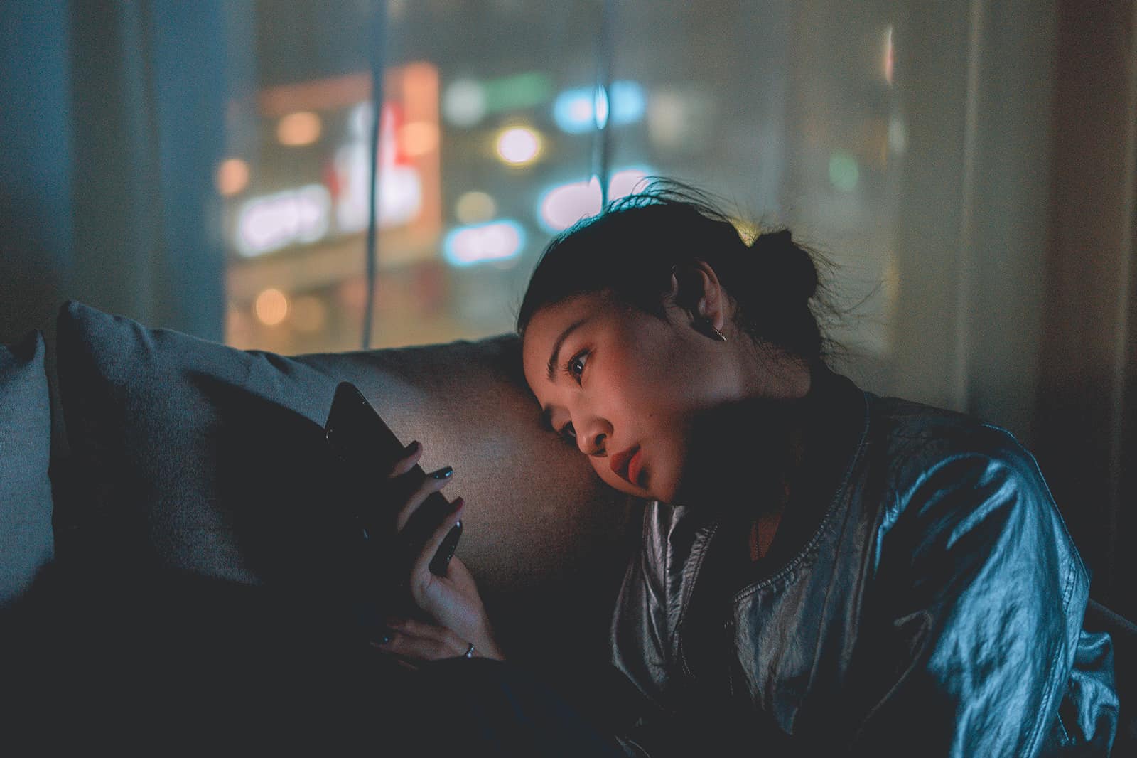 eine traurige Frau, die ein Smartphone betrachtet, das im Dunkeln auf der Couch sitzt