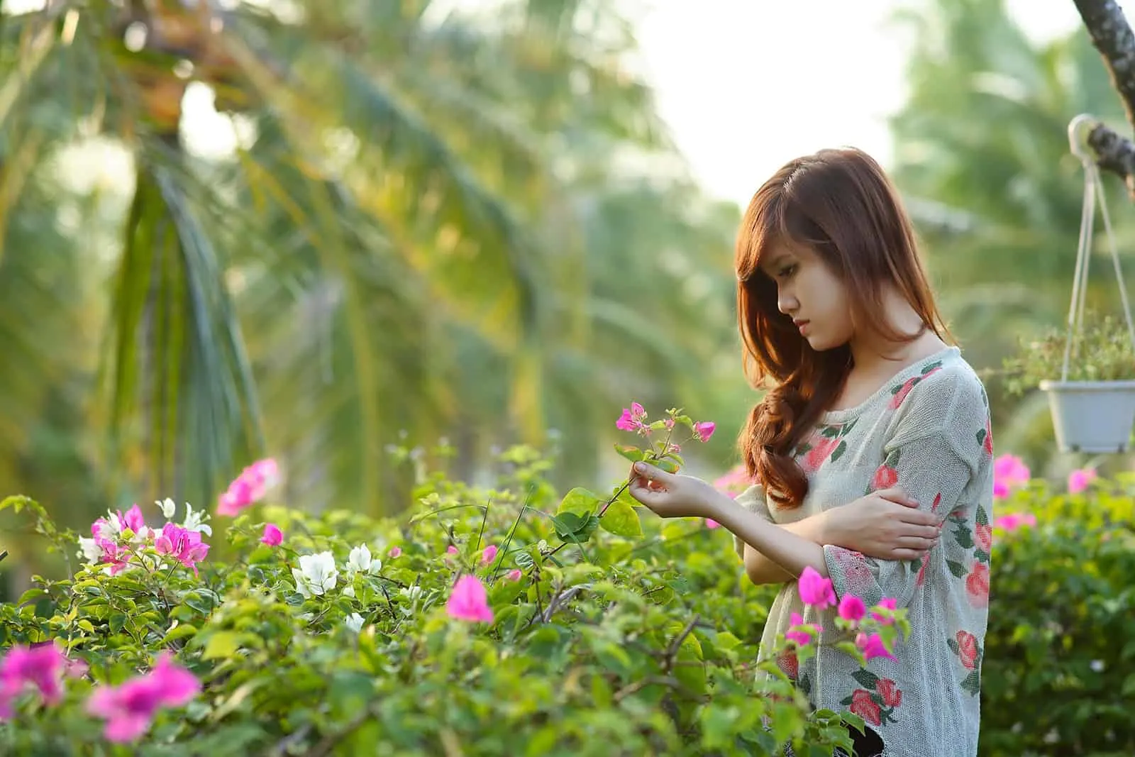 eine traurige Frau, die rosa Blumen berührt, die im Garten stehen