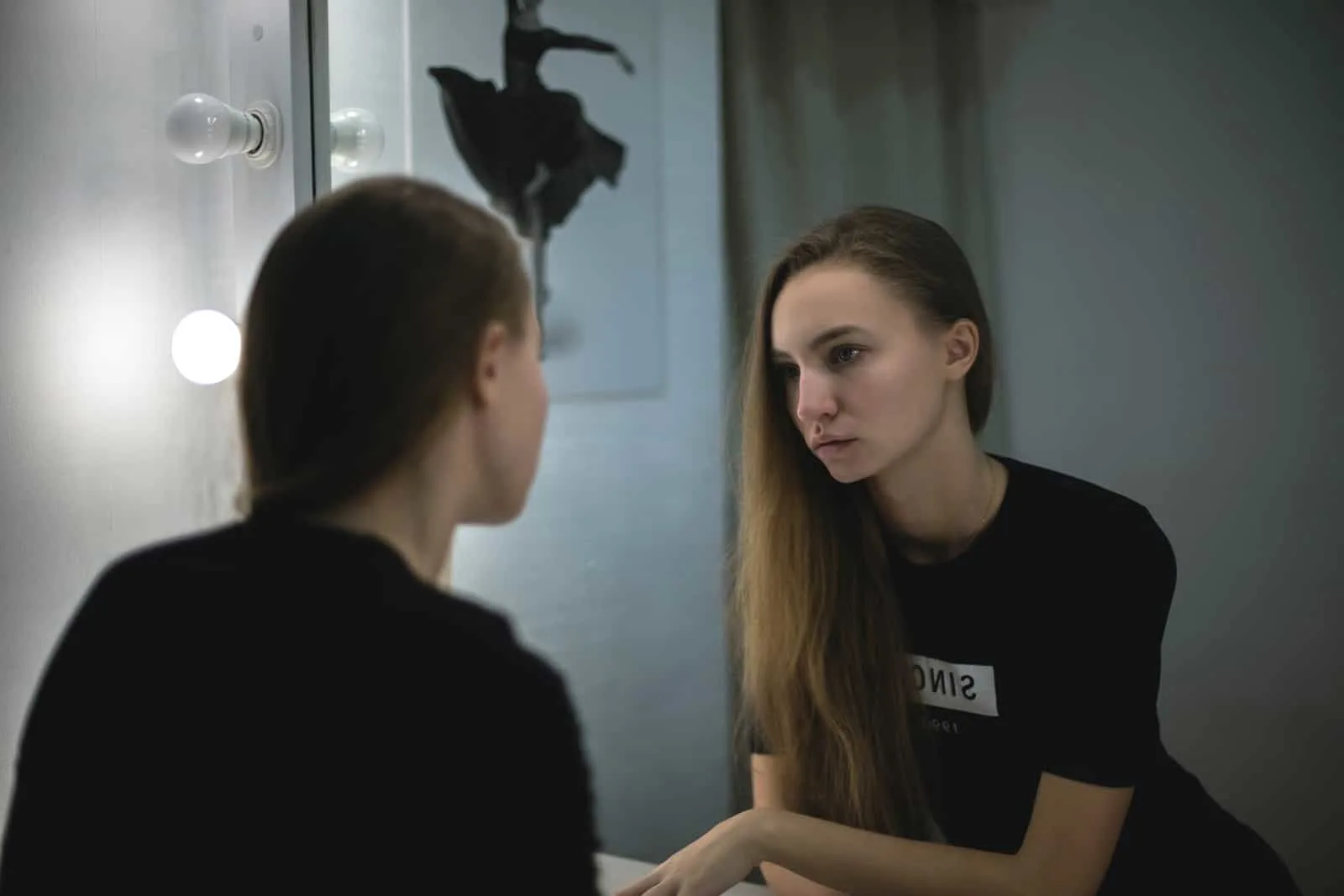 eine traurige Frau in einem schwarzen T-Shirt, die sich in den Spiegel schaut