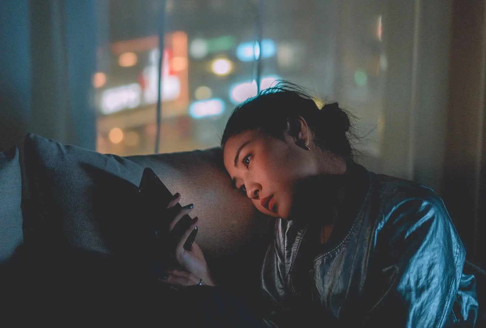 eine traurige Frau, die ihr Smartphone benutzt, während sie im Dunkeln sitzt