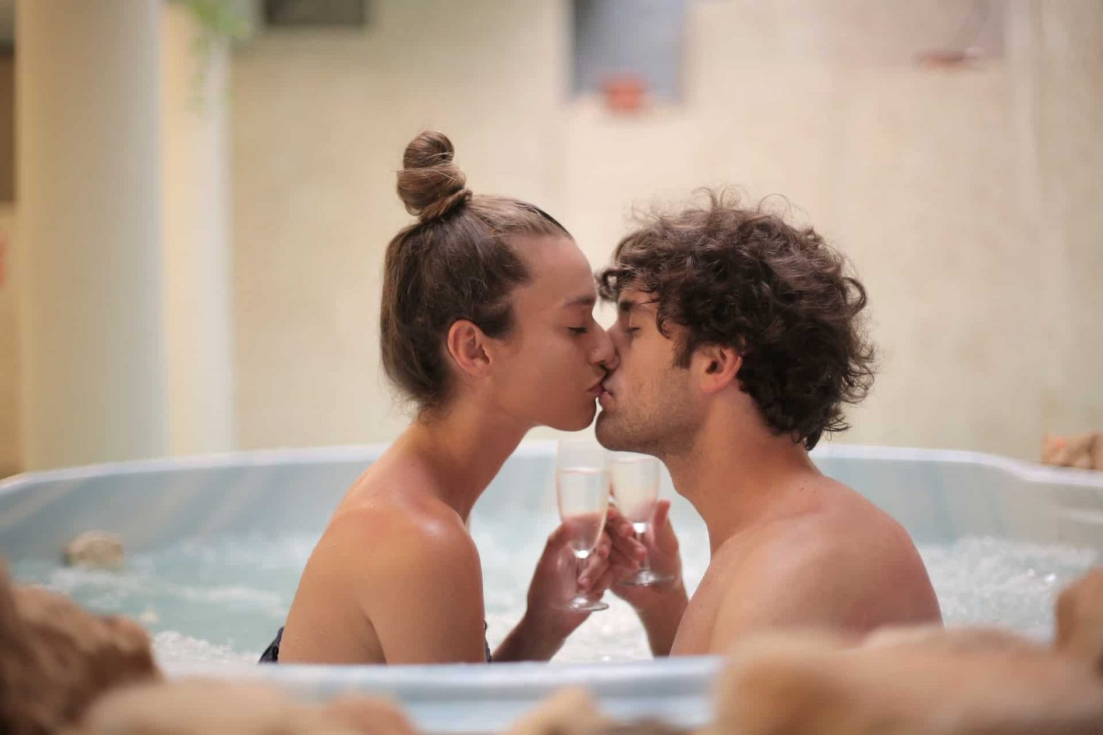 glückliches Paar, das in einem Whirlpool küsst und ein Glas Champagner hält