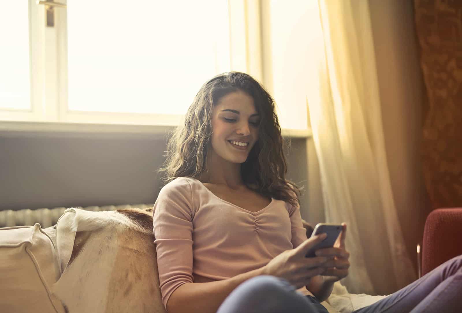 lächelnde Frau mit einem Smartphone auf der Couch zu Hause sitzen