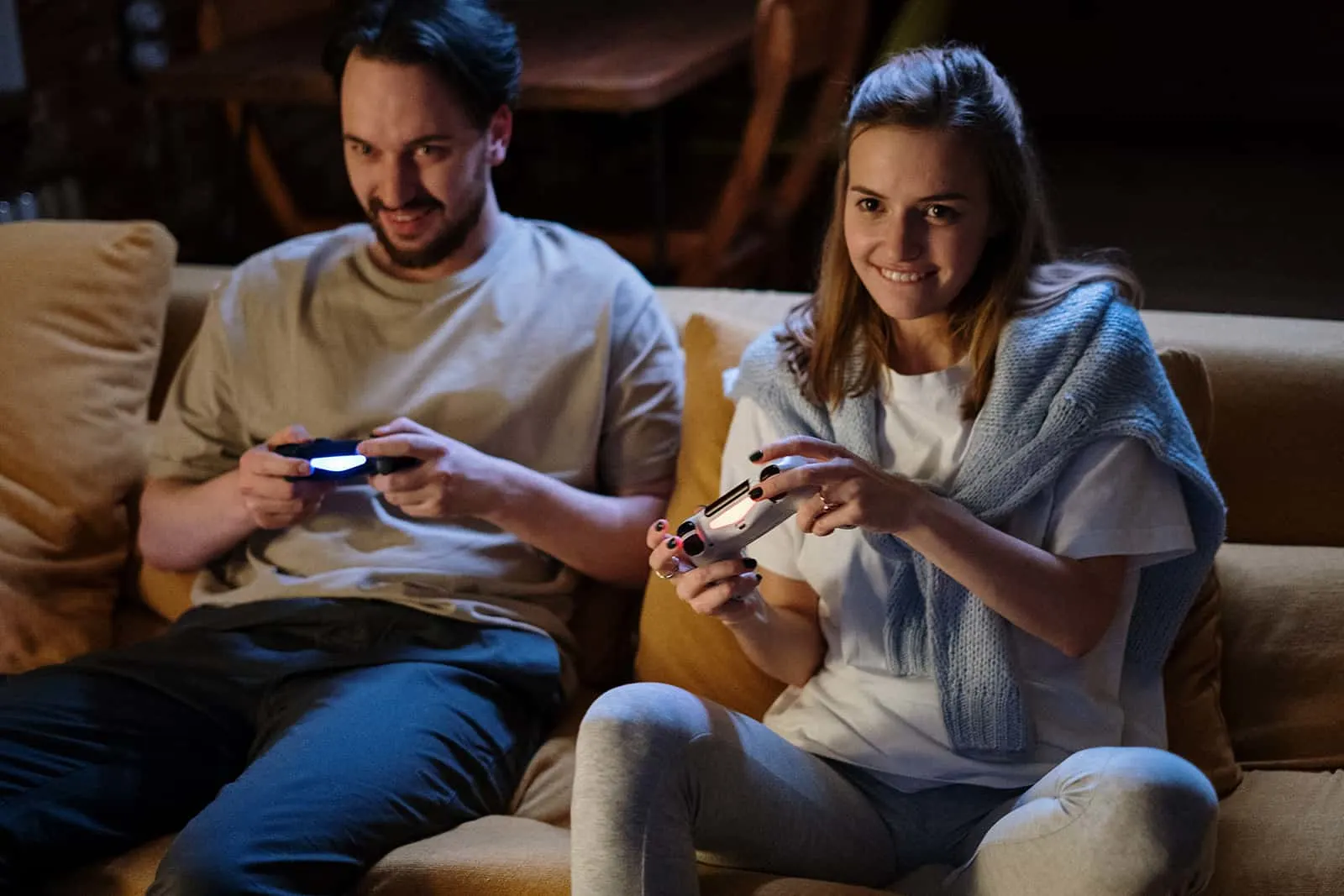 lächelndes Paar, das Konsolen für Videospiele hält, die auf der Couch sitzen
