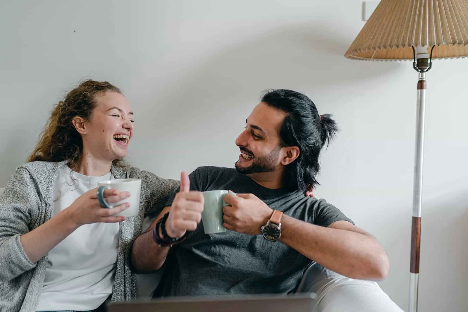 lachender Mann und Frau, die Kaffee trinken, der zu Hause auf der Couch sitzt