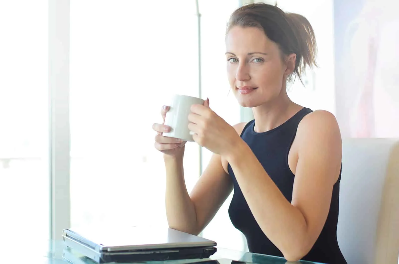 positive Frau, die eine Tasse Kaffee hält, die im Büro sitzt