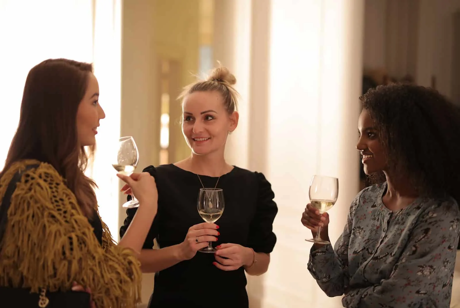 Drei Frauen unterhalten sich und halten ein Trinkglas, während sie auf der Party stehen