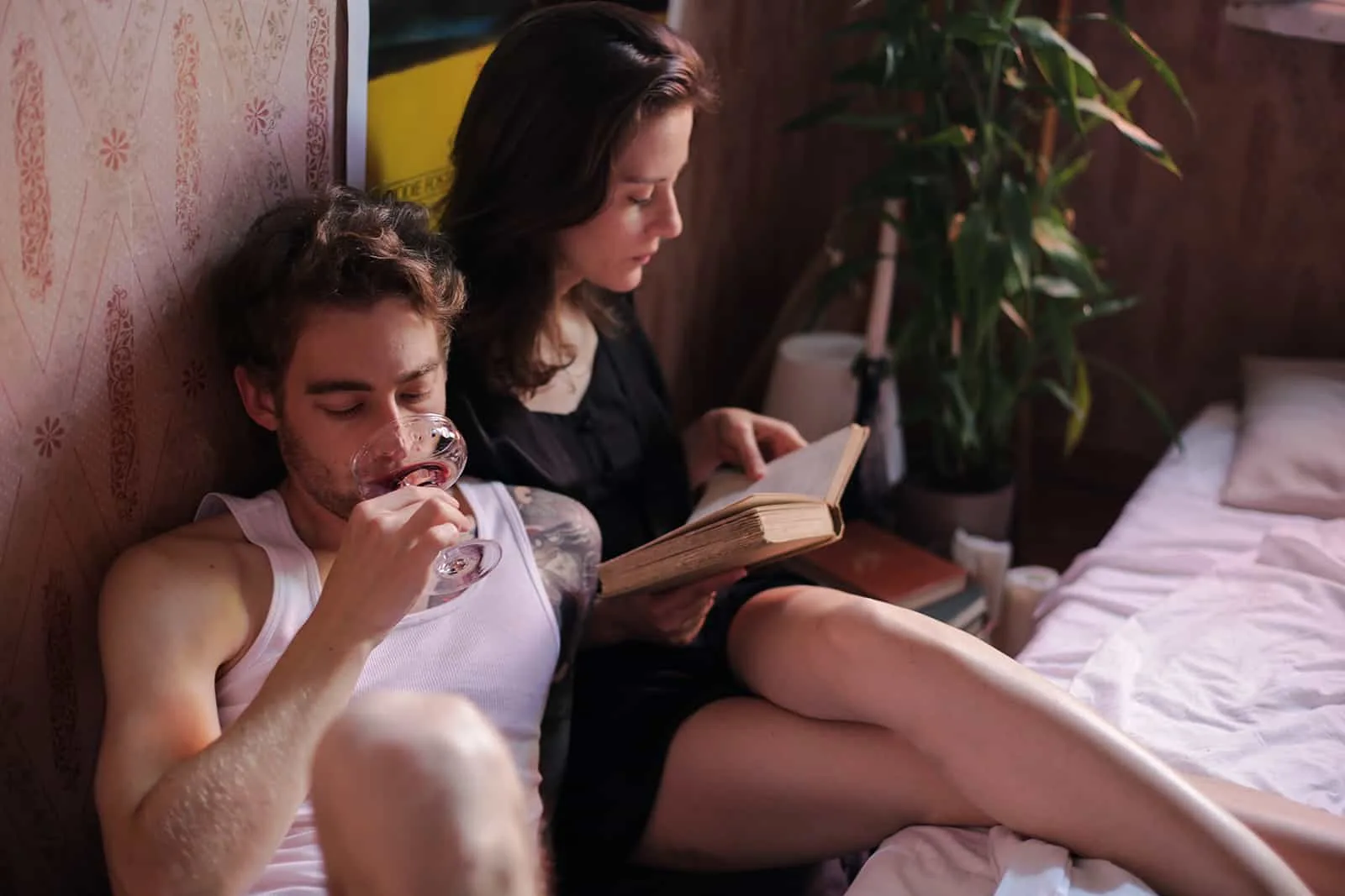 Ein Mann trinkt Wein und eine Frau liest ein Buch, während sie neben einem Bett sitzt