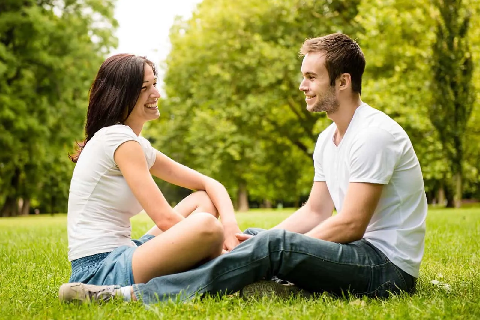 Ein lächelnder Mann und eine lächelnde Frau sitzen sich im Gras gegenüber