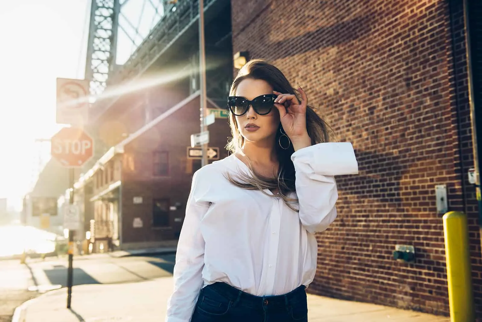 Frau berührt ihre Sonnenbrille, die alleine auf dem Bürgersteig geht