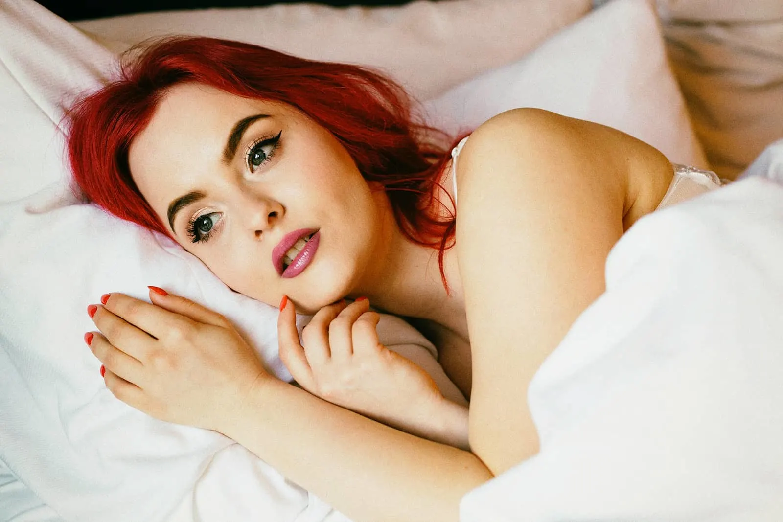 Frau mit roten Haaren, die im Bett liegt und nachdenkt