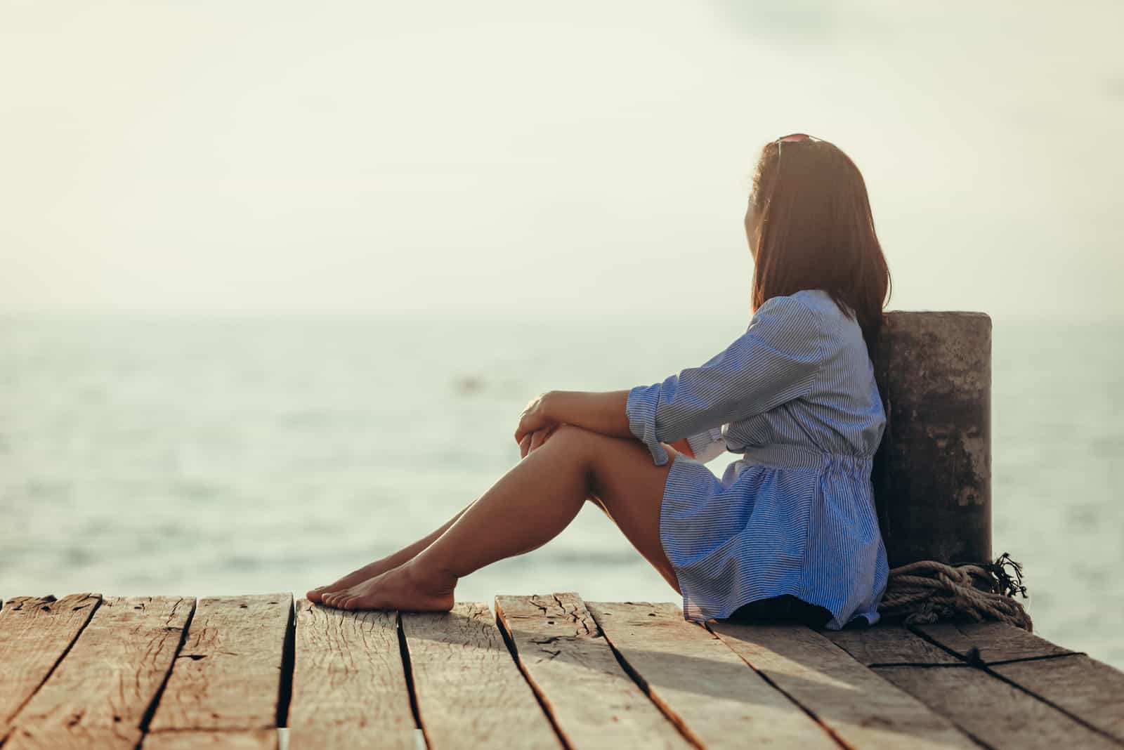 Frau sitzt allein einsam auf Holzbrücke