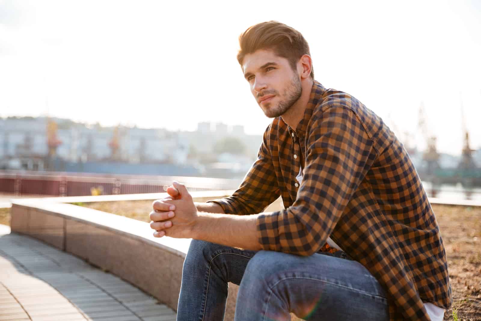 Nachdenklicher junger Mann im karierten Hemd, der draußen sitzt und denkt