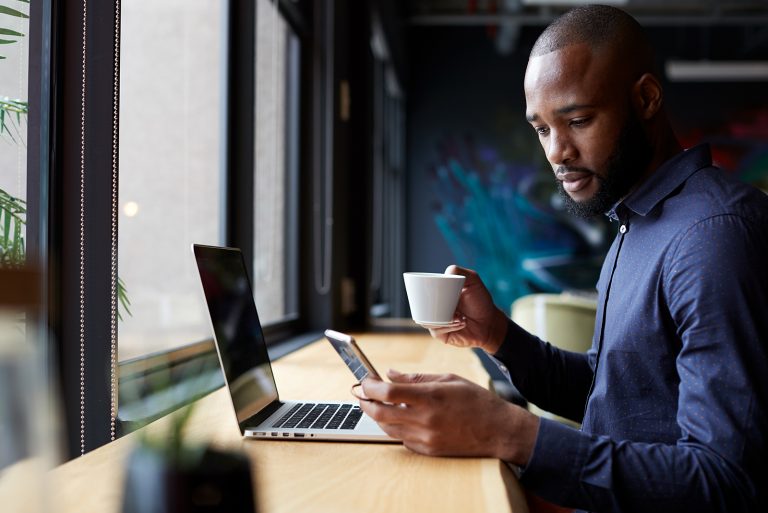 Ein Mann, der im Café sitzt und sein Smartphone überprüft