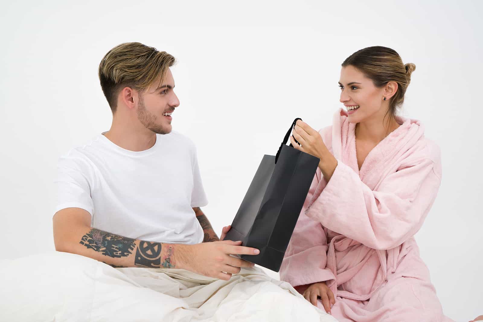Ein Mann, der ein Geschenk von seiner Freundin erhält, während er in einem Bett sitzt