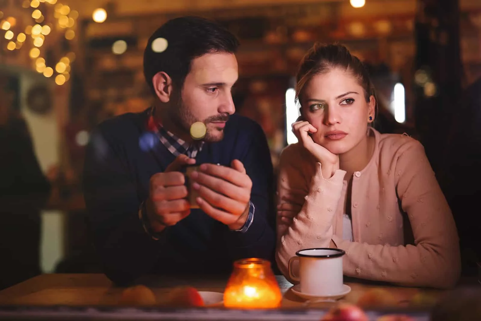 ein Mann, der eine nachdenkliche Frau betrachtet, während er zusammen in einem Café sitzt