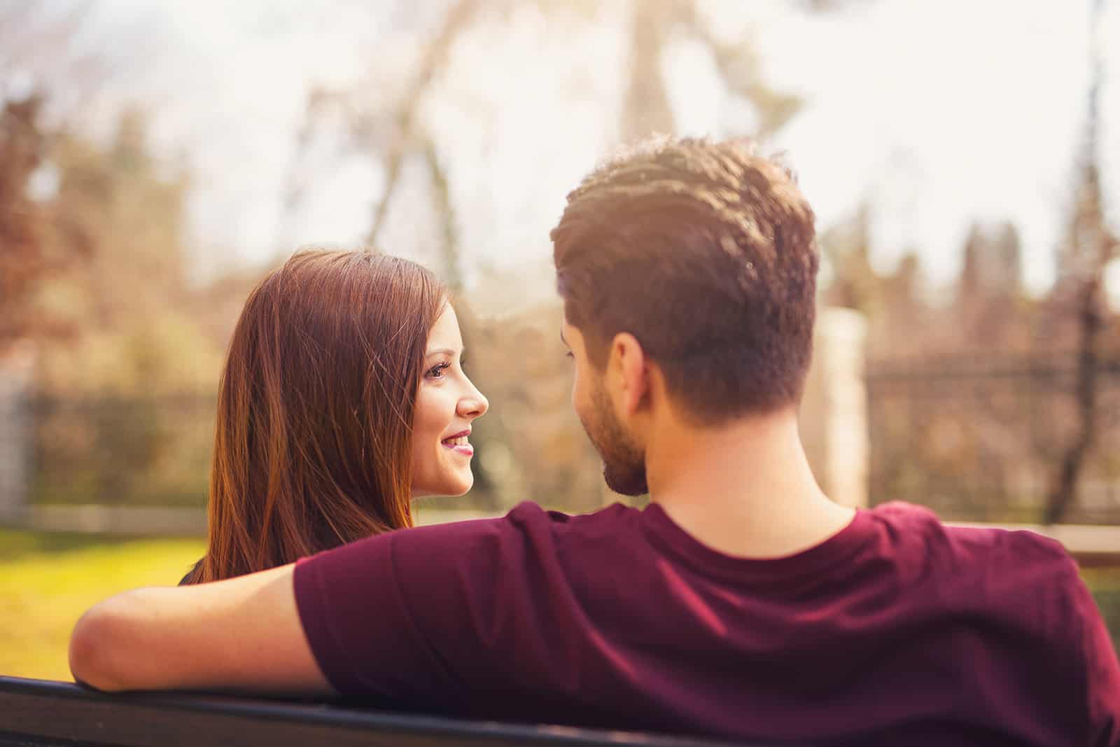 Ein Mann umarmt eine lächelnde Frau, während er zusammen auf der Bank sitzt
