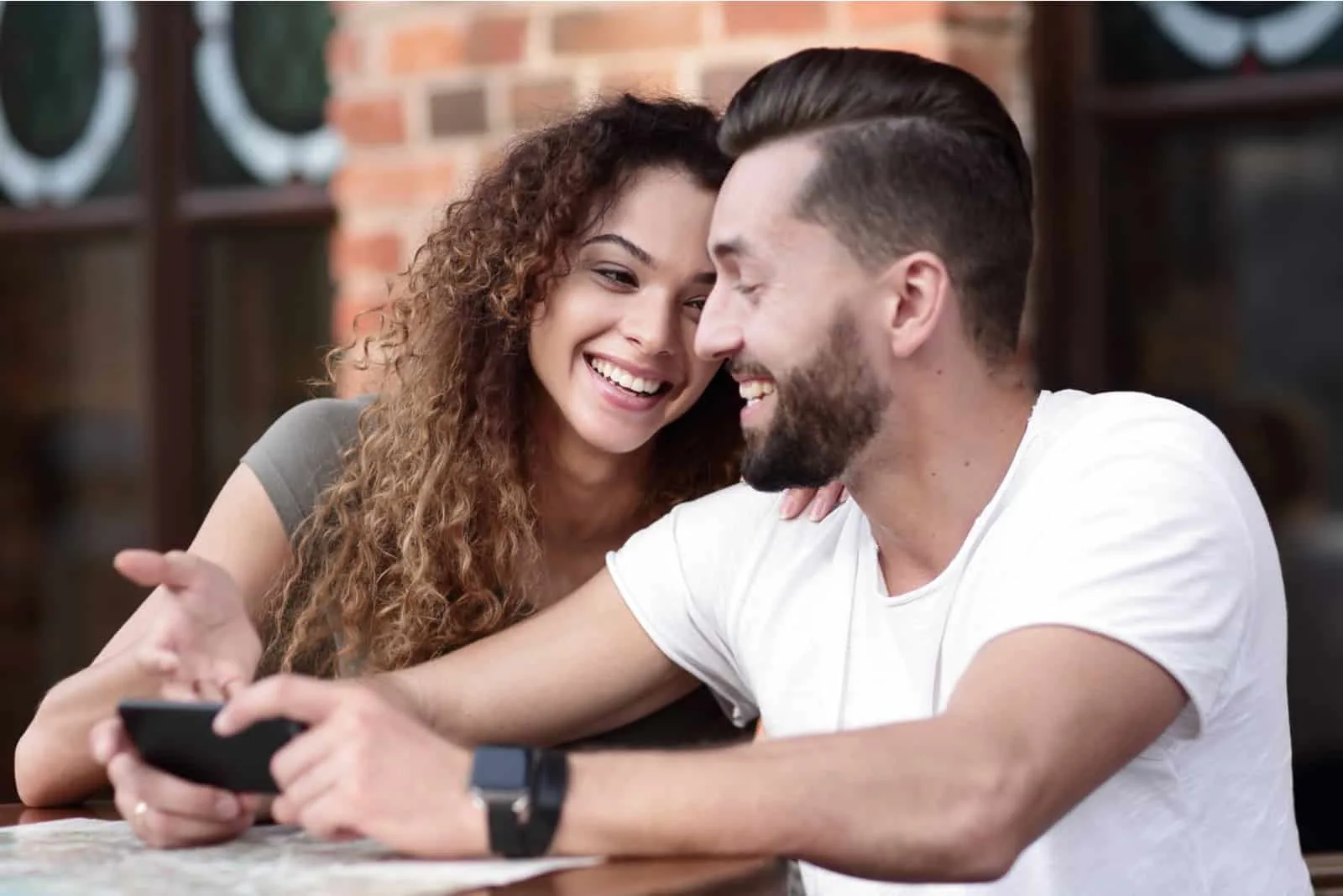 ein glückliches Paar auf der Caféterrasse sitzt und benutzt ein Smartphone