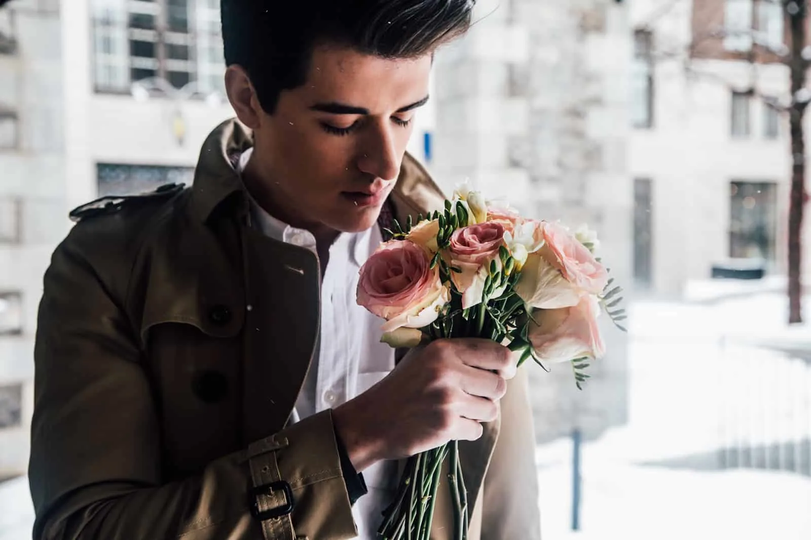 ein hübscher junger Mann, der einen Strauß rosa Rosen hält und daran riecht
