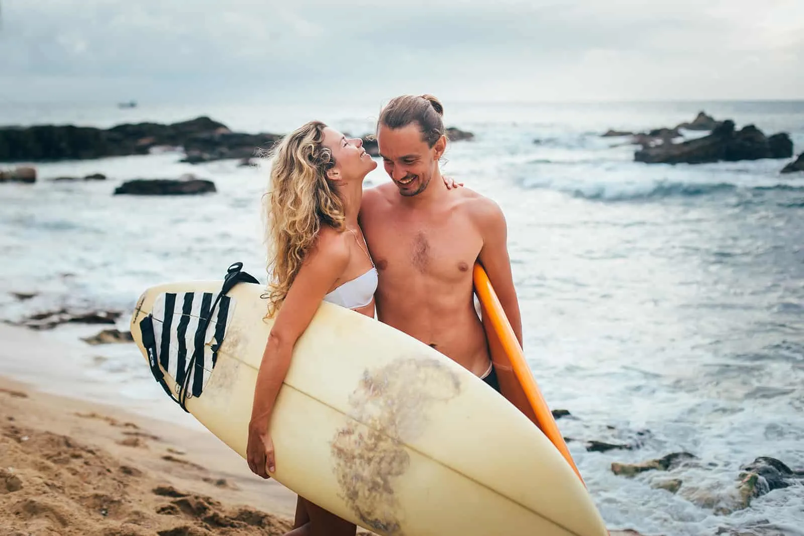 ein liebendes Paar, das Surfbretter hält, die am Strand umarmen