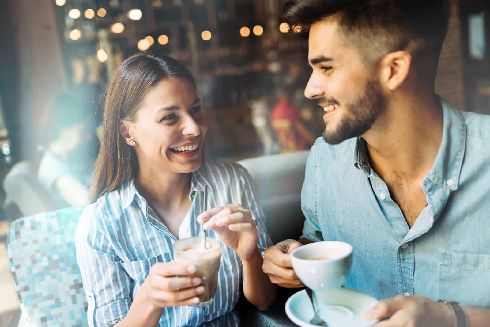 Ein positiver Mann und eine positive Frau sehen sich an, während sie zusammen Kaffee trinken