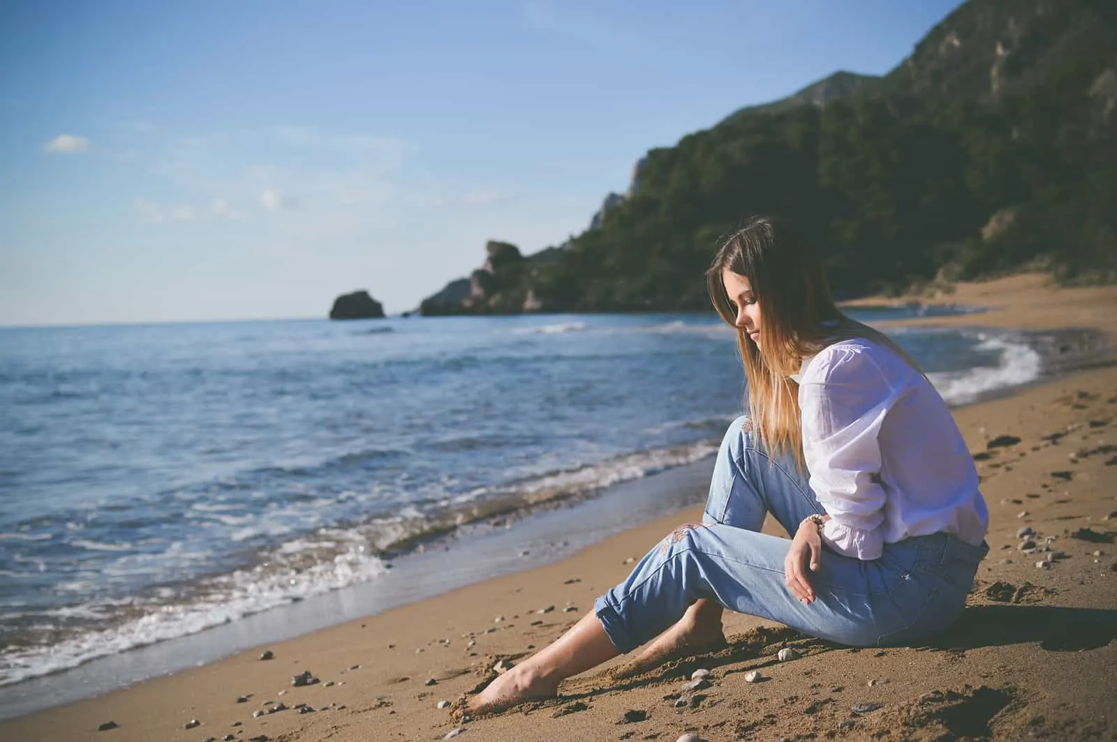 eine Frau, die alleine am Strand sitzt und nachdenklich aussieht