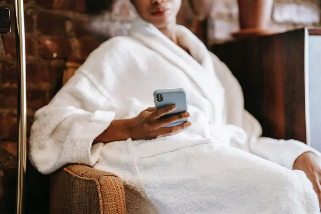 eine Frau im Bademantel, die eine Nachricht auf dem Smartphone tippt, während sie im Sessel sitzt