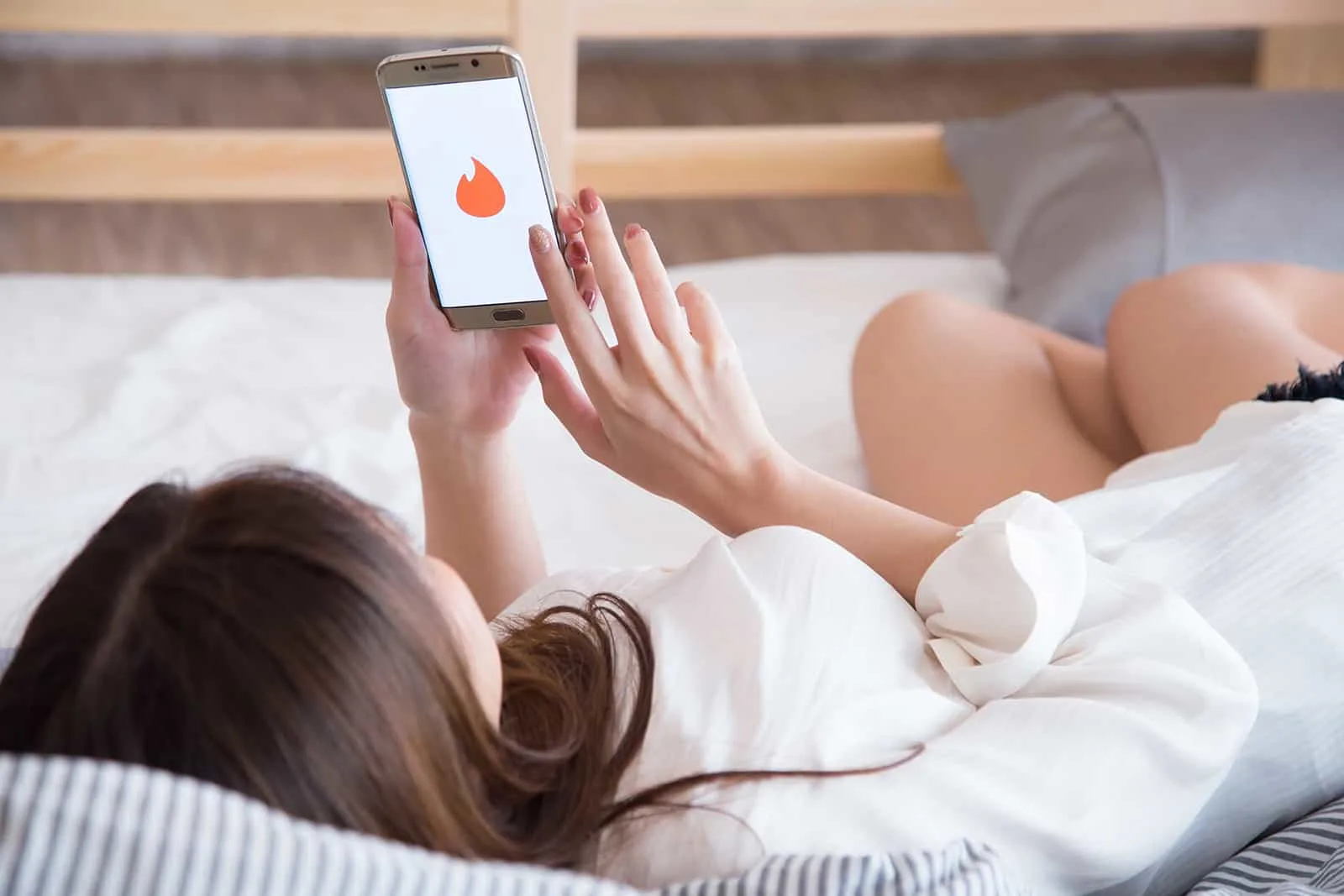 eine Frau mit Dating-App auf einem Smartphone auf dem Bett liegen